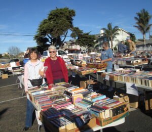 People at a book sale standing with rows of books in boxes